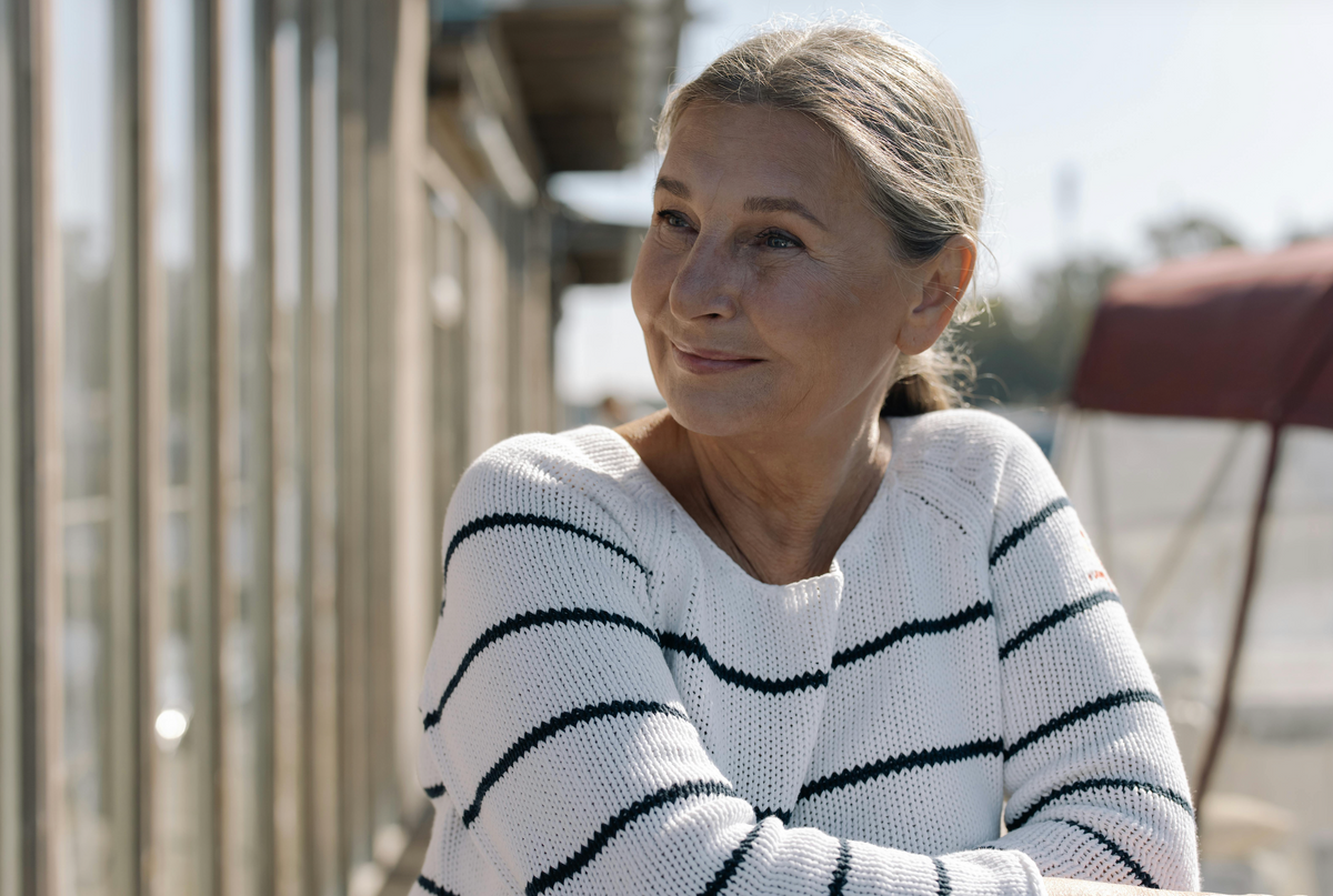 Mature woman in her late 50s seated outdoors in natural light, representing the women VeraTenet supports through the menopausal transition.